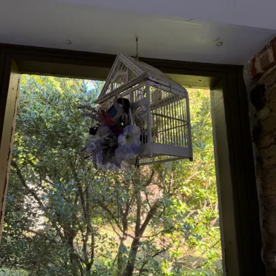 Sale Photo Thumbnail #78: Hanging painted wooden birdcage planter adorned with faux flowers, featuring a rustic house-shaped design.