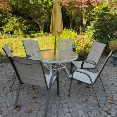 Sale Photo Thumbnail #120: Outdoor patio dining set featuring a round glass-top table, six mesh fabric armchairs, and a yellow market umbrella, set on a stone paver patio.