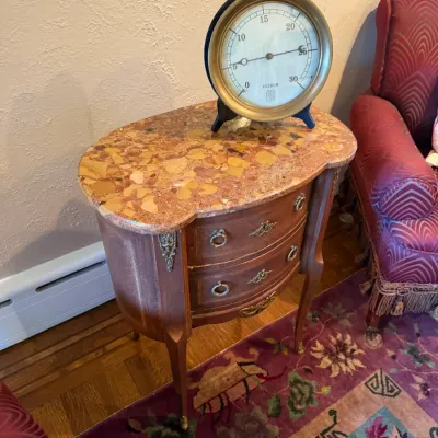 Sale Photo Thumbnail #97: French-style two-drawer side table with a brecciated marble top and ornate brass hardware, paired with a large vintage industrial vacuum gauge.