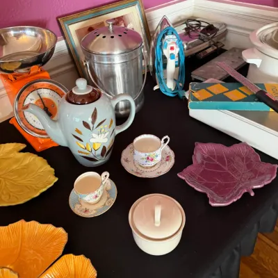Sale Photo Thumbnail #109: Collection of vintage tabletop items including a mid-century Franciscan Autumn ceramic teapot, an orange Hanson kitchen scale, floral teacups with saucers, and colorful leaf-shaped serving dishes.