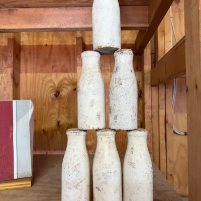 Sale Photo Thumbnail #192: Set of six vintage wooden milk bottle carnival toss game pins, featuring distressed white paint and heavy surface wear.