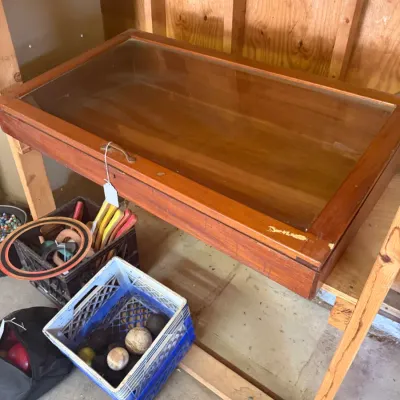 Sale Photo Thumbnail #201: Vintage wood and glass display case featuring a hinged glass top and metal handle, set above crates containing various sports equipment.