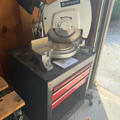 Sale Photo Thumbnail #221: Hitachi 15-inch miter saw mounted on a black and red rolling tool stand.