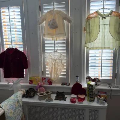 Sale Photo Thumbnail #185: Collection of vintage children's clothing hanging on shutters, alongside a variety of tabletop decor, trinket boxes, and small collectibles.