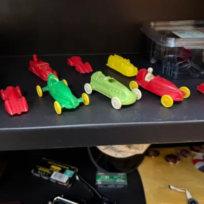 Sale Photo Thumbnail #149: Collection of vintage molded plastic toy cars and race cars displayed on a dark shelf.