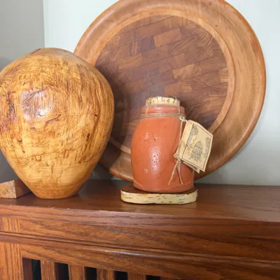 Sale Photo Thumbnail #118: Collection of wooden decorative items including a hand-turned spalted wood vase, a teak parquet round tray, and a small terracotta crock resting on a birch slice.