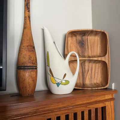 Sale Photo Thumbnail #119: Collection of decorative items including an antique wooden Indian club, a mid-century modern ceramic pitcher with abstract geometric graphics, and a carved wooden divided tray.