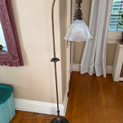 Sale Photo Thumbnail #141: Vintage bridge arm floor lamp featuring a distressed bronze-tone finish, ornate round base, and a fluted clear glass shade.