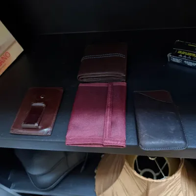 Sale Photo Thumbnail #151: Collection of men's wallets and small leather goods, including a bifold wallet, a money clip card holder, a maroon nylon wallet, and a sleeve case.