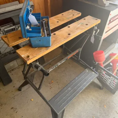Sale Photo Thumbnail #220: Vintage Black & Decker Workmate folding workbench project center with a small blue plastic toolbox resting on top, showing minor surface wear from use.