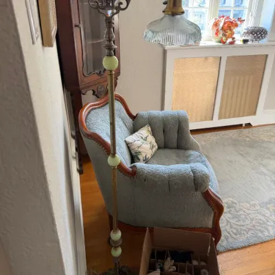 Sale Photo Thumbnail #136: Vintage bridge arm floor lamp featuring a fluted glass shade, ornate brass details, and pale green jadeite marble accents, set beside a blue upholstered armchair.
