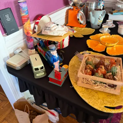 Sale Photo Thumbnail #107: A table displaying eclectic collectibles including a cast iron Uncle Sam mechanical bank, vintage kitchenware, yellow leaf-shaped serving dishes, and small gourds in a wooden crate.