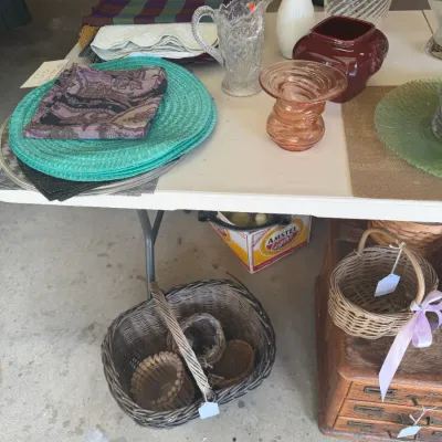 Sale Photo Thumbnail #209: Collection of tabletop glassware, ceramics, and textiles, including pressed glass pitchers, a milk glass vase, colorful place mats, and woven baskets.