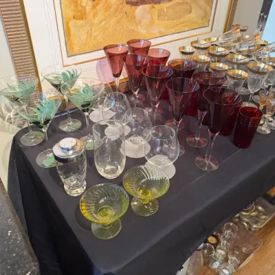 Sale Photo Thumbnail #160: Large assortment of vintage glassware on a table, including cranberry stemware, gold-rimmed glasses, hand-painted martini glasses, glass cocktail shaker, and yellow Vaseline-style dessert dishes.