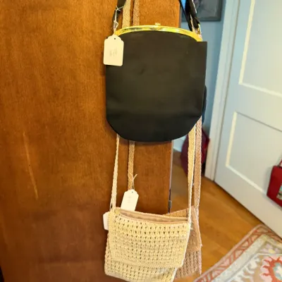 Sale Photo Thumbnail #166: Vintage black purse with a gold-tone clasp frame and black shoulder strap, hanging alongside two woven crochet crossbody bags.