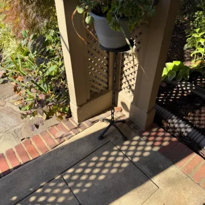 Sale Photo Thumbnail #176: Tall wrought iron plant stand with chain-link central support, holding a potted plant on a porch.