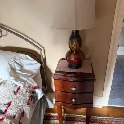 Sale Photo Thumbnail #140: Traditional dark wood nightstand with two drawers and silver hardware, topped with a colorful gourd-shaped ceramic lamp with an off-white shade.