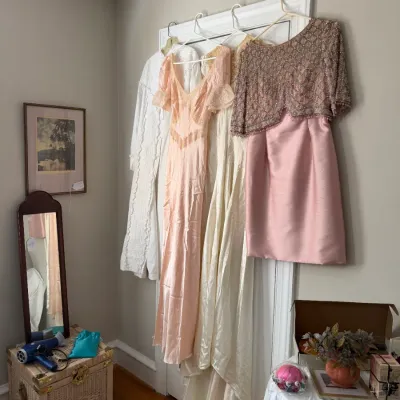 Sale Photo Thumbnail #184: Collection of vintage women's formal dresses, including a bead-embellished pink dress and a satin gown, displayed hanging on a door frame.