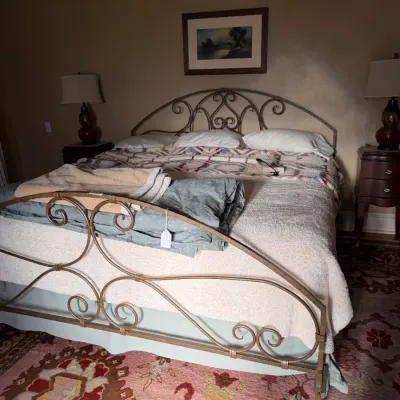 Sale Photo Thumbnail #143: Wrought iron scrollwork bed frame with mattress, bedding, and price tag attached, accompanied by matching nightstands and a patterned area rug.