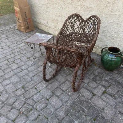 Sale Photo Thumbnail #197: Rustic woven twig sleigh-style chair, displayed outdoors alongside a small metal side table and a green glazed ceramic urn.