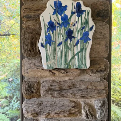 Sale Photo Thumbnail #80: Hand-painted ceramic tile wall art panel featuring vibrant blue iris flowers on a white background, mounted on a stone pillar.