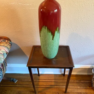 Sale Photo Thumbnail #95: Tall ceramic floor vase with a glossy red upper glaze and textured green lower section, displayed on a small wooden side table.
