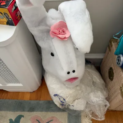 Sale Photo Thumbnail #189: Plush white rabbit mascot costume head featuring floppy ears and a pink flower accent, stored in plastic.