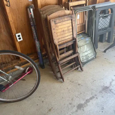 Sale Photo Thumbnail #216: Collection of folded chairs including vintage slatted wooden folding chairs and metal folding chairs leaning against a garage wall.