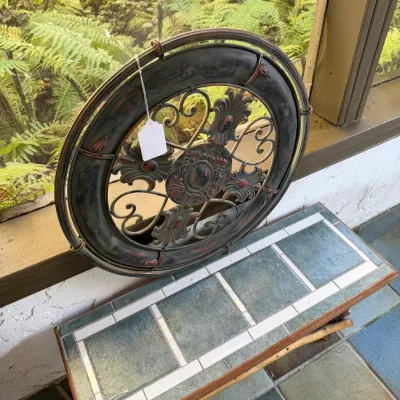 Sale Photo Thumbnail #88: Circular wrought metal medallion wall art piece with a distressed dark finish, resting on a tiled-top low bench or table.