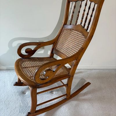 Vintage wooden rocking chair featuring a woven cane seat and backrest with scrolled armrests and spindle accents.