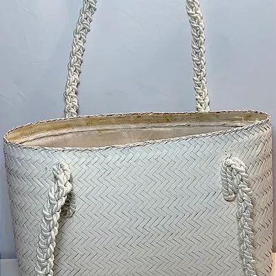 Vintage white woven straw tote handbag with braided cord shoulder straps, showing light discolouration around the inner rim.