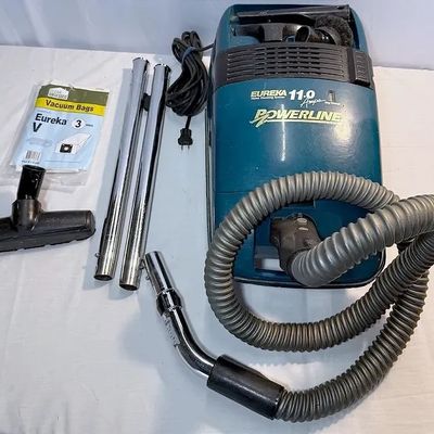 Vintage teal Eureka Powerline 11.0 Amps canister vacuum cleaner with hose, extension wands, attachments, and a pack of replacement bags.