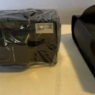 Mikona MV-828 35mm point-and-shoot camera, wrapped in plastic packaging alongside its original black carrying case.