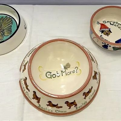 Trio of hand-painted ceramic pet bowls, featuring playful dog illustrations, text details, and whimsical designs.