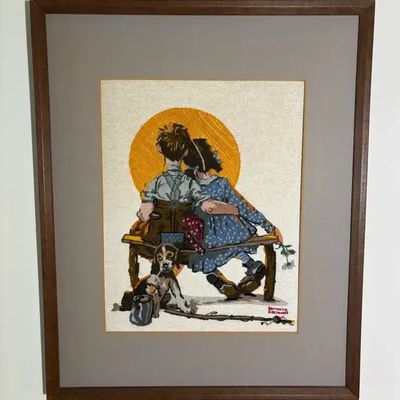 Framed embroidery stitchery art featuring Norman Rockwell's "Boy and Girl Gazing at Sunset" with a dog, set under glass in...