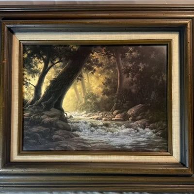 Framed oil painting depicting a forest stream with sunlight filtering through dense trees, set in a heavy rustic wood frame with a linen...