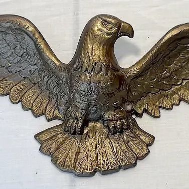 Vintage cast metal eagle wall plaque with spread wings and a distressed gold-toned finish.