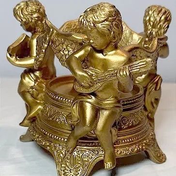 Gold-toned cast metal or resin candle holder featuring musical cherubs playing instruments around a ornate pedestal base.