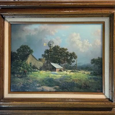 Framed painting depicting a rural landscape with a farmhouse, windmill, and bluebonnet field, housed in a heavy rustic wood frame.