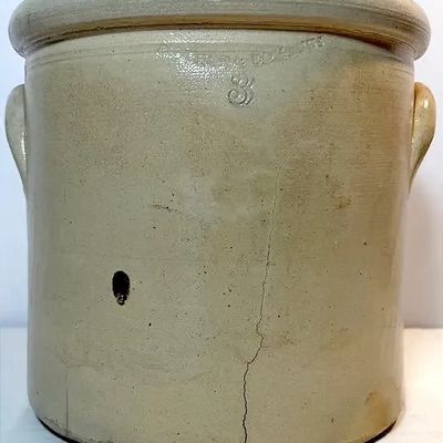 Antique 3-gallon stoneware crock with side handles and impressed markings, showing a prominent vertical crack along the lower front.