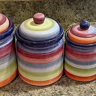 Set of four hand-painted ceramic kitchen canisters featuring colorful horizontal stripes and ball knobs on the lids.