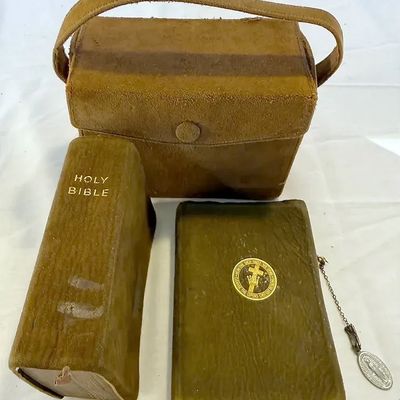Vintage tan leather Bible carrying case set with a handle, featuring two small religious Bibles and an attached Miraculous Medal pendant.