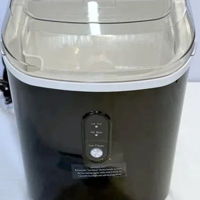Modern black portable countertop ice maker featuring a carrying handle, transparent lid, control panel, and an included white ice scoop.