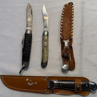 Collection of vintage pocket knives and fixed-blade hunting knives with leather sheaths, showing varied wear and patina.