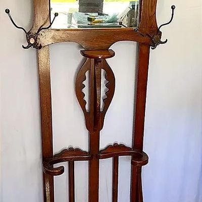 Antique carved oak hall tree featuring a centered rectangular mirror, metal coat hooks, small shelf, and integrated umbrella stand base.