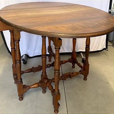 Antique gateleg drop-leaf dining table crafted from stained wood, featuring turned spindle legs and stretchers.