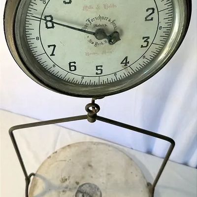 Antique hanging scale by Chas. Forschner & Sons, featuring a round glass-covered dial with black numerals and a lower circular pan.