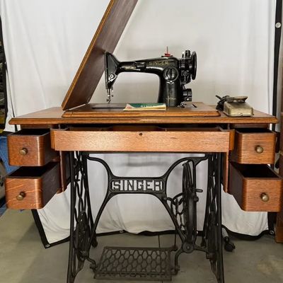 Vintage Singer sewing machine built into a wooden treadle cabinet with cast iron base and four side drawers.