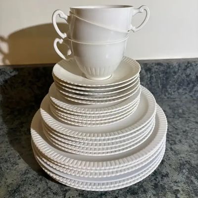 Stacked white porcelain dinnerware set with fluted borders, including dinner plates, salad plates, saucers, and teacups.