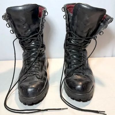 Pair of men's black leather tall lace-up work or combat boots featuring D-ring hardware and heavy-duty treaded soles, showing minor...